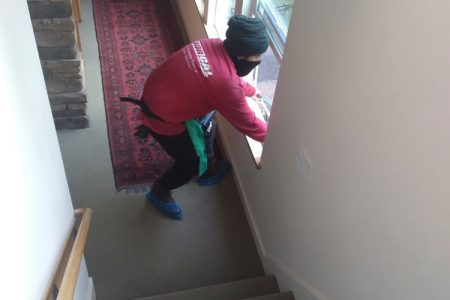 A person from NorCal Maintenance Inc. cleaning a window in a residential space in Windsor, wearing a red shirt and blue shoe covers.