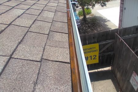 A clean gutter running along the edge of a roof next to a wooden fence and a sign marked "Security Checkpoint 12."