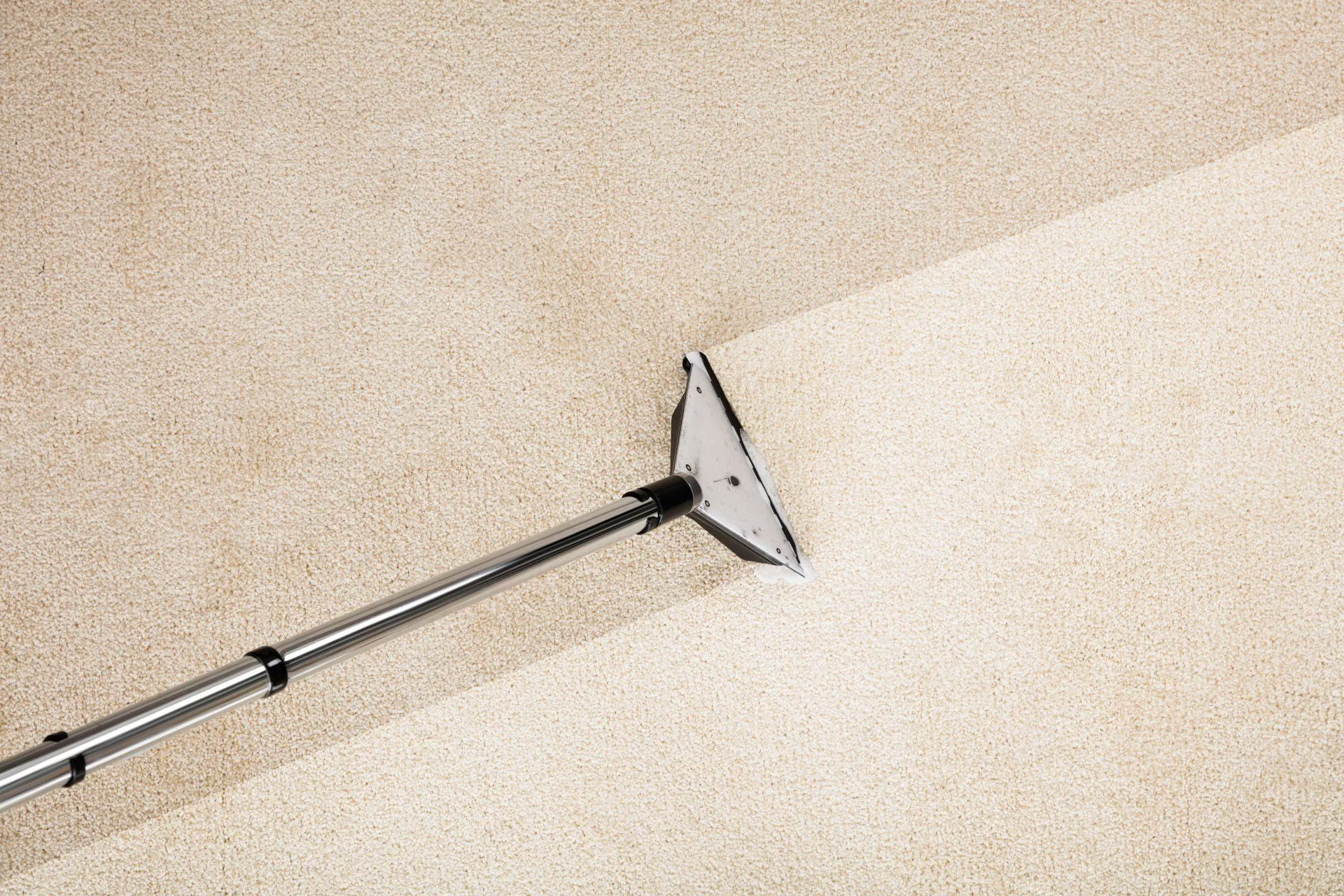A carpet cleaning wand is shown partially cleaning a beige carpet, highlighting the clear difference between the cleaned and uncleaned sections.