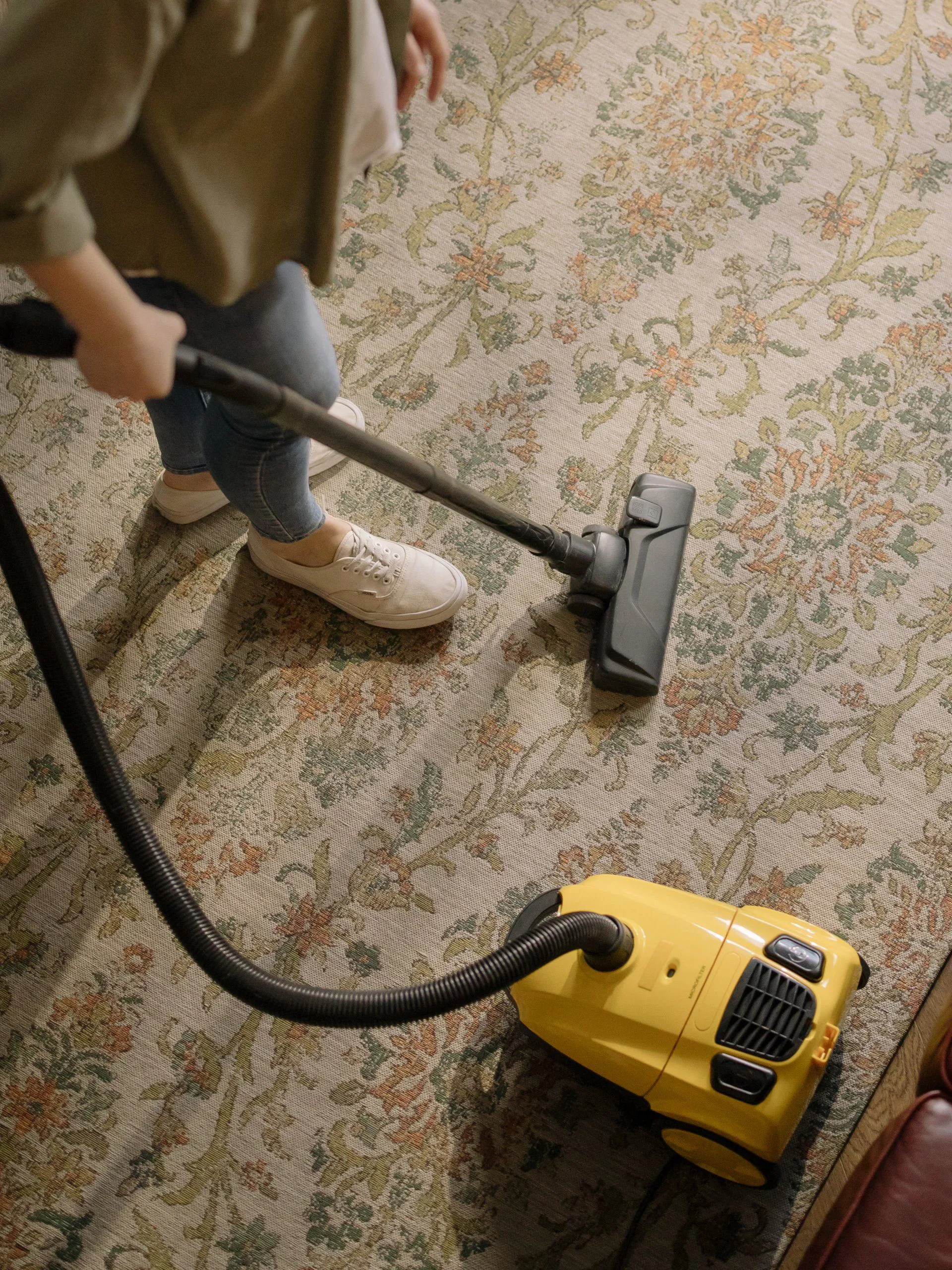 A person vacuuming a floral-patterned carpet with a yellow vacuum cleaner, emphasizing carpet cleaning services in Cotati by North Coast Carpet Care, Inc.