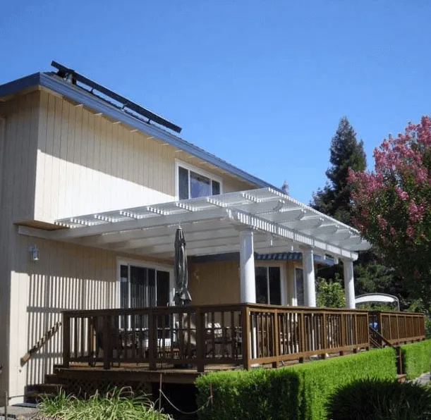 A house in Santa Rosa featuring a wooden deck with a white pergola built by Northwest Exteriors, surrounded by greenery and clear blue skies.
