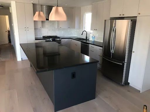 A modern kitchen remodel with a large black island countertop, stainless steel appliances, and pendant lighting, completed by NuHome Remodeling in San Jose.