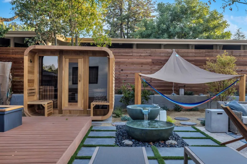 A beautifully landscaped backyard featuring a wooden sauna, a hammock under a canopy, and a modern water feature, designed by NuHome Remodeling in San Jose.