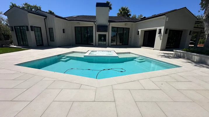 A modern house with a pristine pool and surrounding patio, showcasing the work of Olivera Pool Services in San Jose, under a clear blue sky.