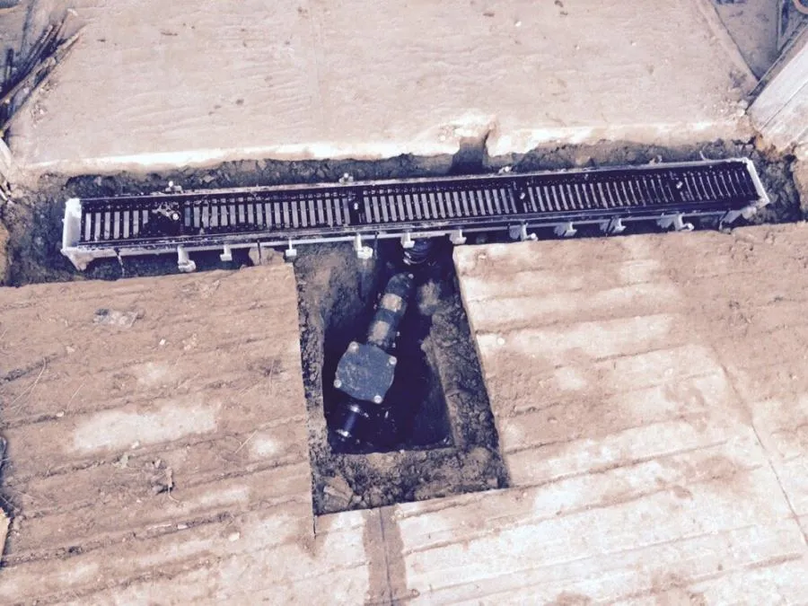 A trench drain system and connected plumbing pipe partially embedded in a cut-out section of a cement floor.