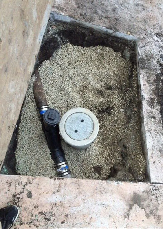 "A plumbing setup partially buried in gravel, installed by One Source Plumbing and Rooter, Inc. in San Francisco, featuring a pipe with connectors and a round access point."