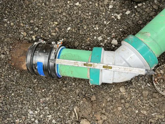 Close-up image of a green plumbing pipe with a level tool over it, surrounded by gravel, showing precise alignment work by Oro Pro Plumbing, Inc.