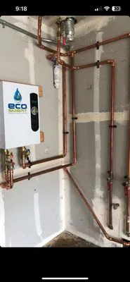 Wall-mounted plumbing system with copper pipes and a white rectangular control unit, installed by Oro Pro Plumbing, Inc. in South San Francisco.