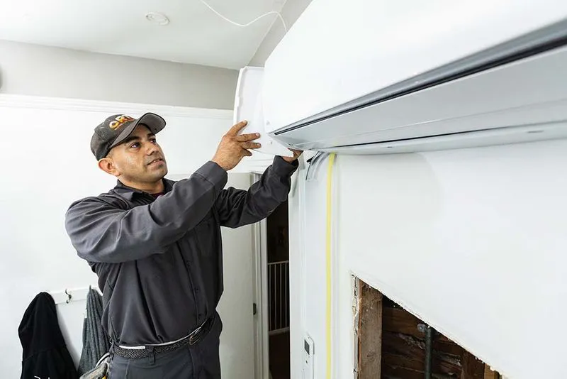 A technician from Ortiz Heating and Air Conditioning in Burlingame installs an air conditioning unit on a wall.