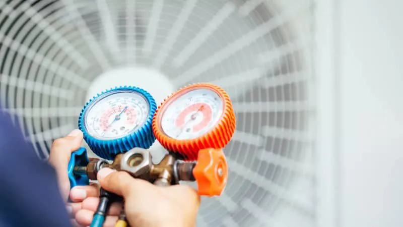 Technician using pressure gauges to measure HVAC system performance in front of a fan unit.