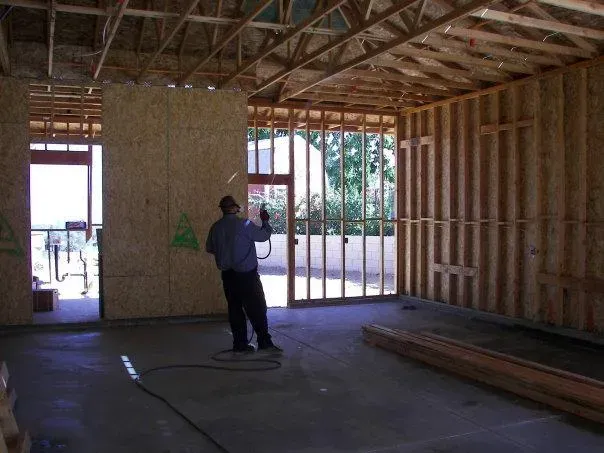 A worker in a partially constructed building in Fremont, applying termite control treatment from Pacific Coast Termite.