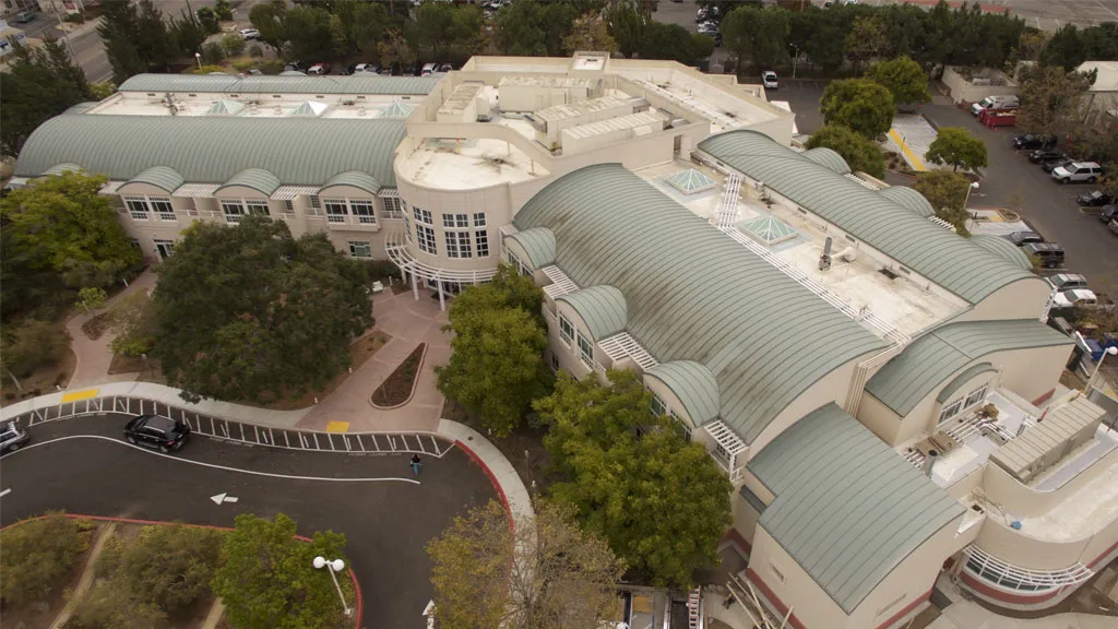 Aerial view of a large, modern building with curved green roofs surrounded by trees and parking spaces, showcasing Pacific Exterior's architectural work in Santa Cruz.