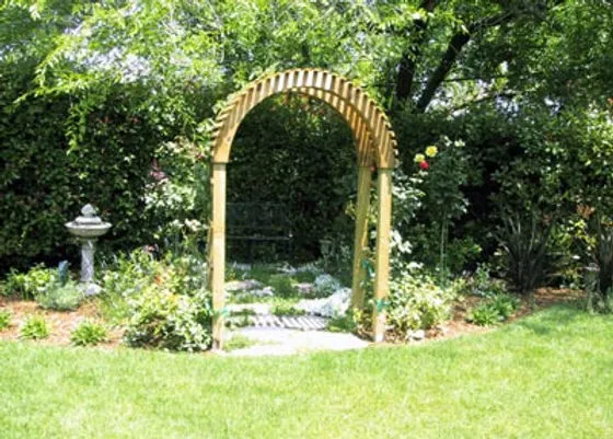 A wooden garden arch surrounded by lush greenery and blooming flowers, with a bird bath nearby, creating a tranquil garden scene.