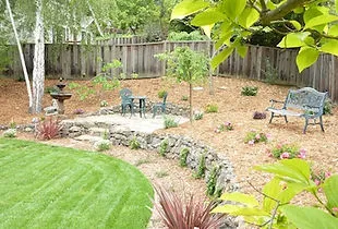 A landscaped backyard with a patio set, stone edging, lawn, and flowering plants, designed by Pacific Landscaping in Walnut Creek.