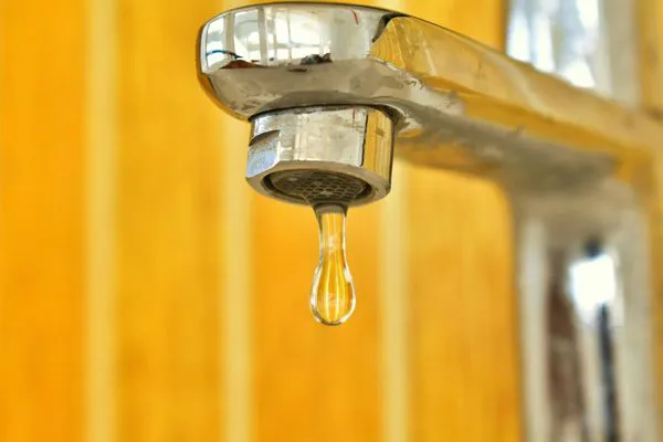 Close-up of a faucet with a droplet of water hanging from the spout, highlighting plumbing services.