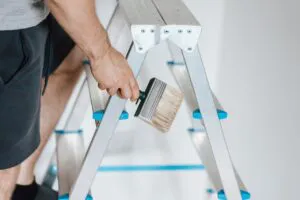 "Person holding a paintbrush on a ladder, ready to paint, representing Paintmasters in Concord."
