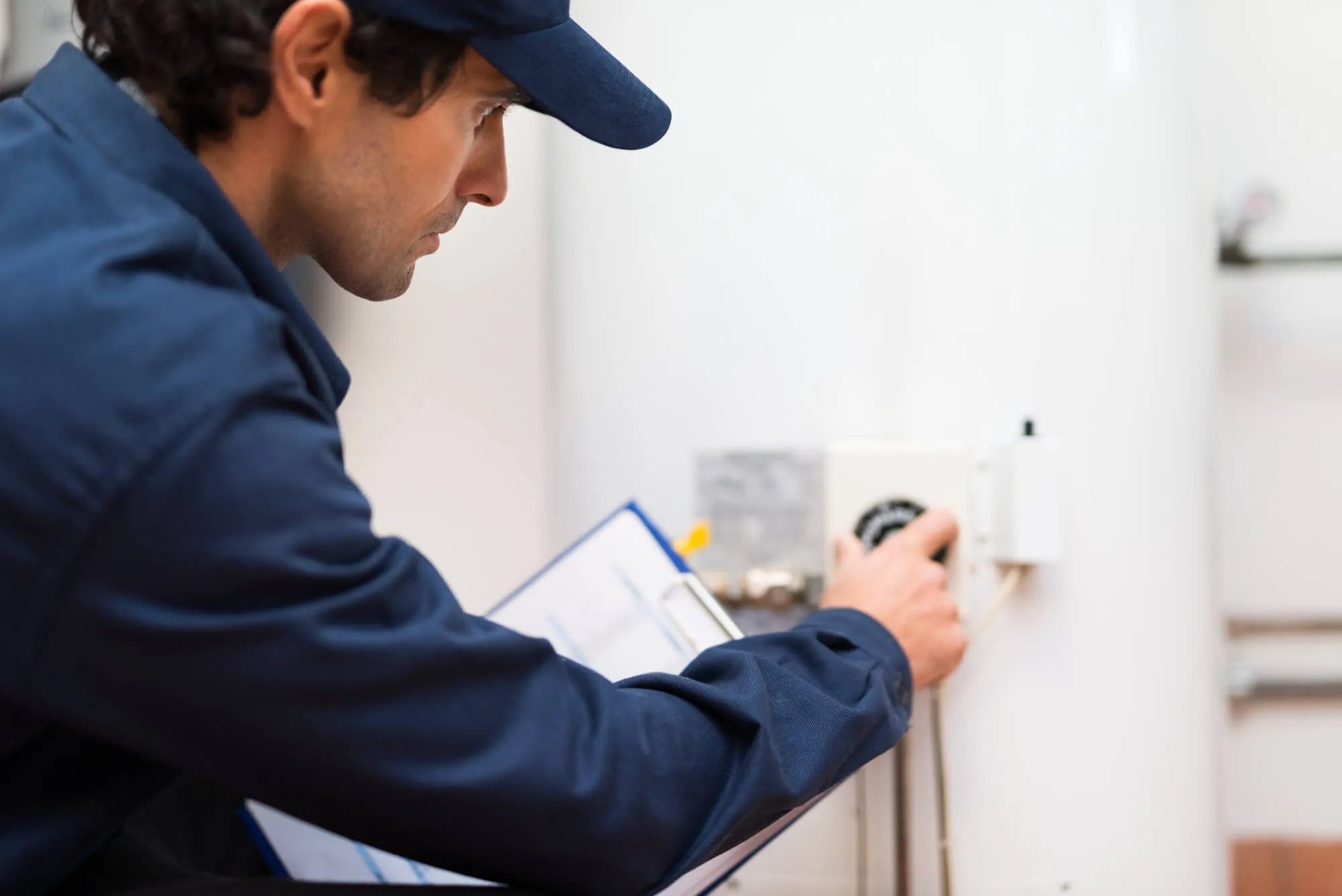 A technician in a blue uniform adjusting a control panel on a heating system.