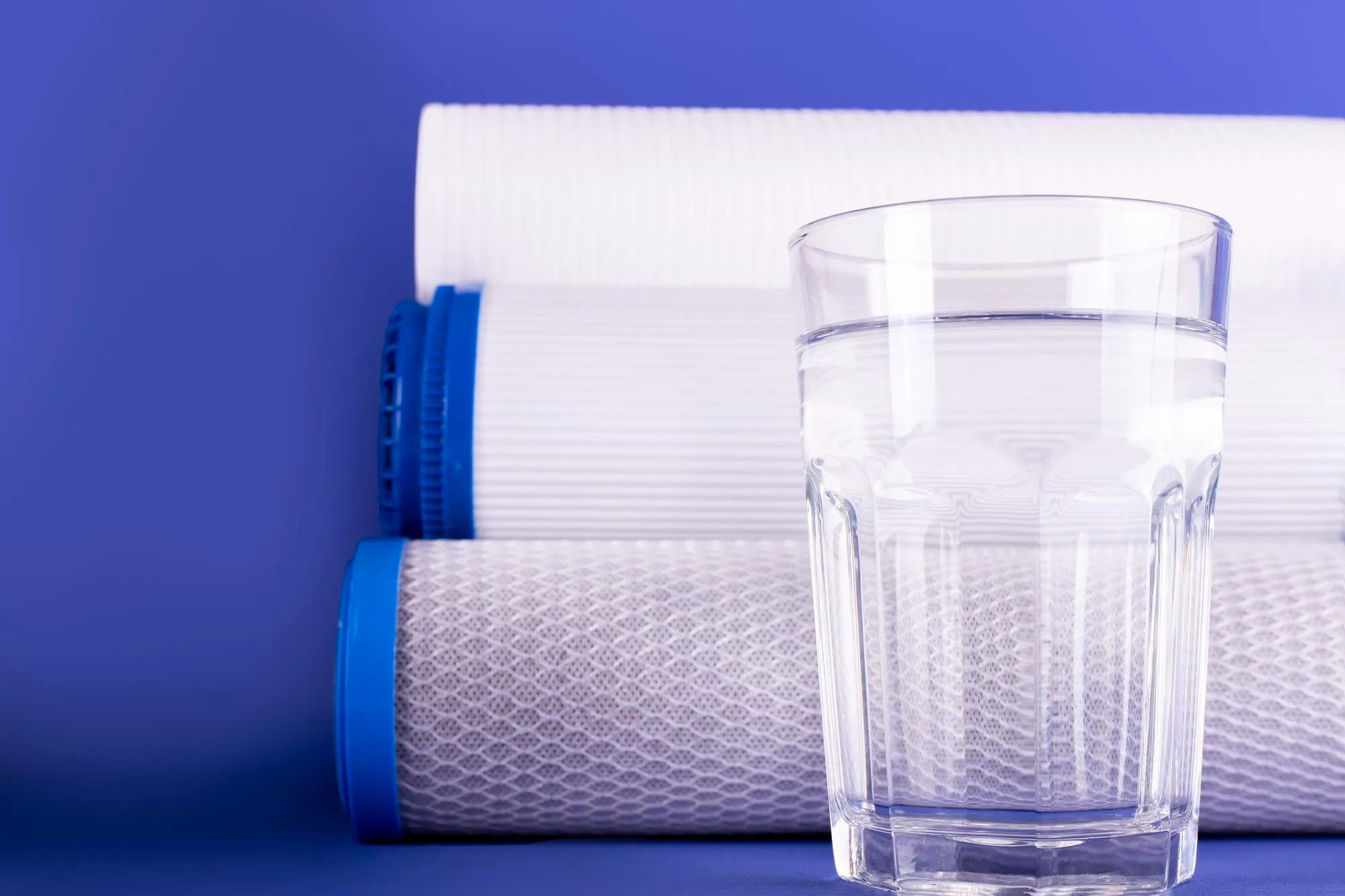 "A clear glass of water is placed in front of three stacked water filters, showcasing water filtration by Paso Robles Plumbing, Heating, and Air in Paso Robles."