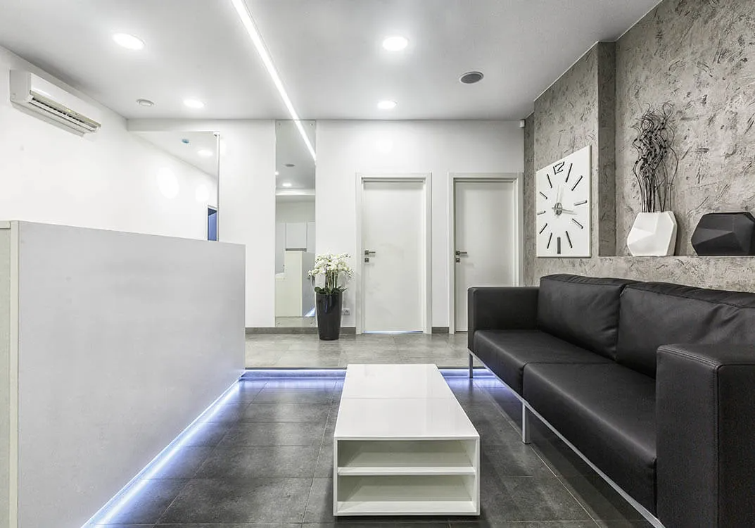 A modern, minimalist office reception area with a sleek black sofa, white coffee table, and contemporary wall clock, designed by Peninsula Design and Construction in Hayward.