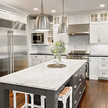 A modern kitchen with white cabinets, stainless steel appliances, and a marble island, designed by Peninsula Design and Construction in Hayward.