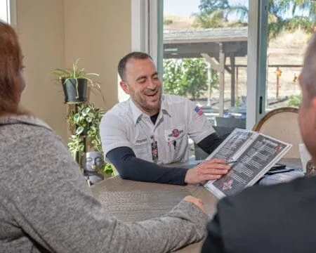 A technician from Perfect Star Heating and Air Conditioning in Concord discusses service options with two customers at a table.