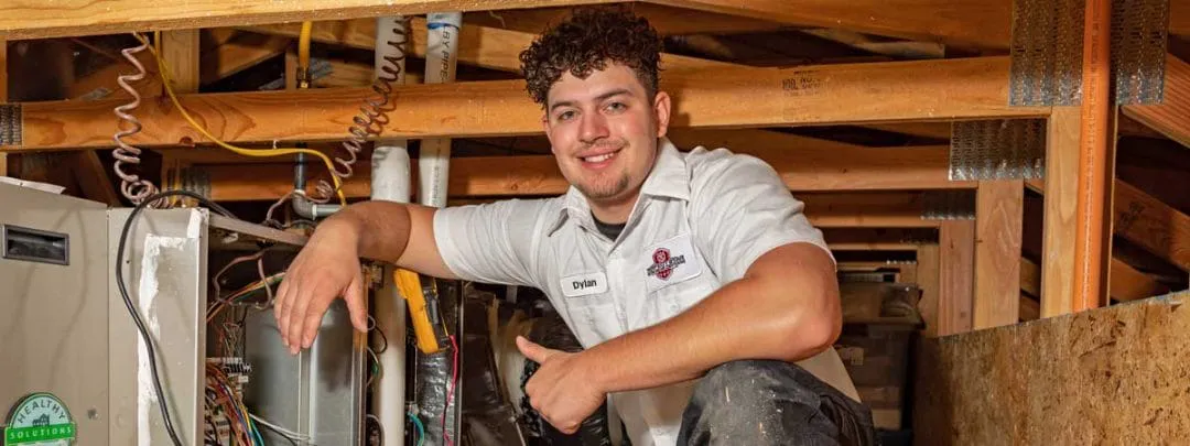 A technician from Perfect Star Heating and Air Conditioning, smiling and giving a thumbs-up while servicing an HVAC unit in an attic.