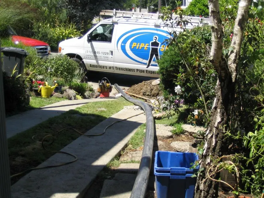 A Pipe Spy Inc. service van parked near a garden while performing a trenchless pipe repair in Berkeley, with a long pipe extending across the lawn.