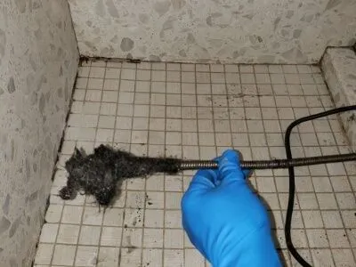 A gloved hand removing a hair clog from a shower drain, showcasing effective plumbing work by Plumbtree Plumbing and Rooter Inc. in Santa Clara.