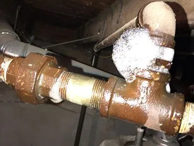 Close-up of a rusted, leaking pipe joint in a basement setting.