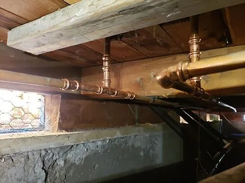 Image of copper pipes installed beneath wooden beams in a basement, showcasing work by Plumbtree Plumbing and Rooter Inc. in Santa Clara.