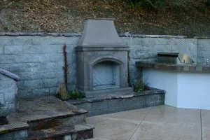 An outdoor patio area featuring a stone fireplace and a built-in grill, designed by Pool & Landscape Development in Brentwood.