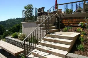 Stone staircase with metal railings, surrounded by landscaped greenery, at a patio area in Brentwood, designed by Pool & Landscape Development.