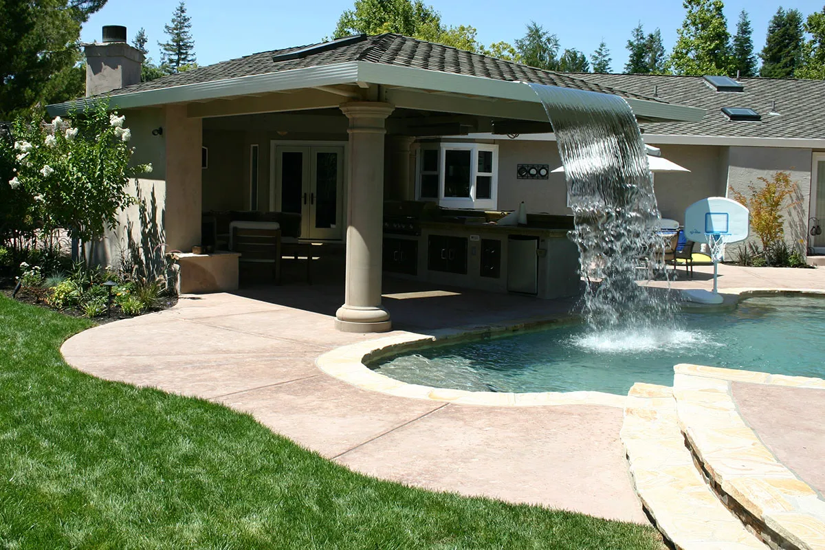 A luxurious backyard in Brentwood featuring a pool with a cascading waterfall, surrounded by manicured landscaping and an outdoor living area.