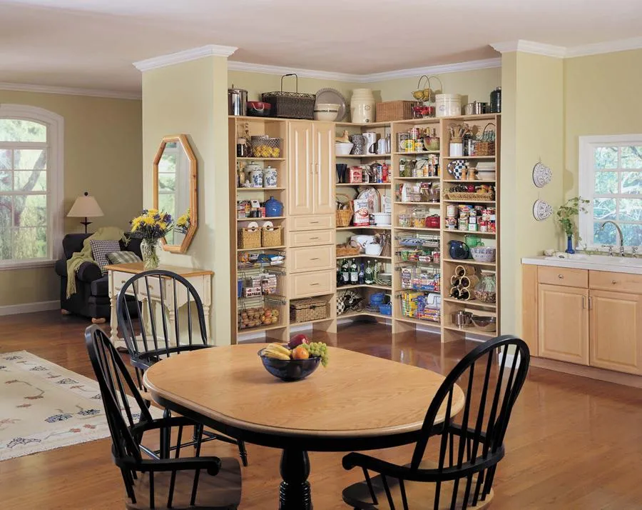 A well-organized kitchen pantry with wooden shelves filled with various food items and decorations, adjacent to a dining area with a wooden table and chairs.