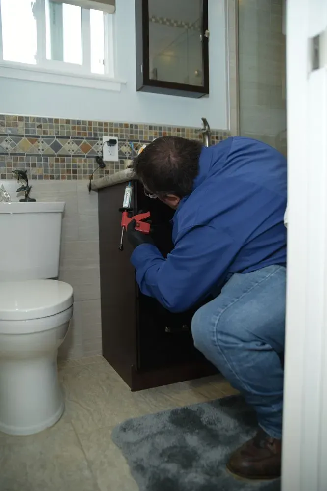 "A pest control technician from Presto Pest Control, Inc. applying pest prevention treatment inside a bathroom cabinet in San Jose."