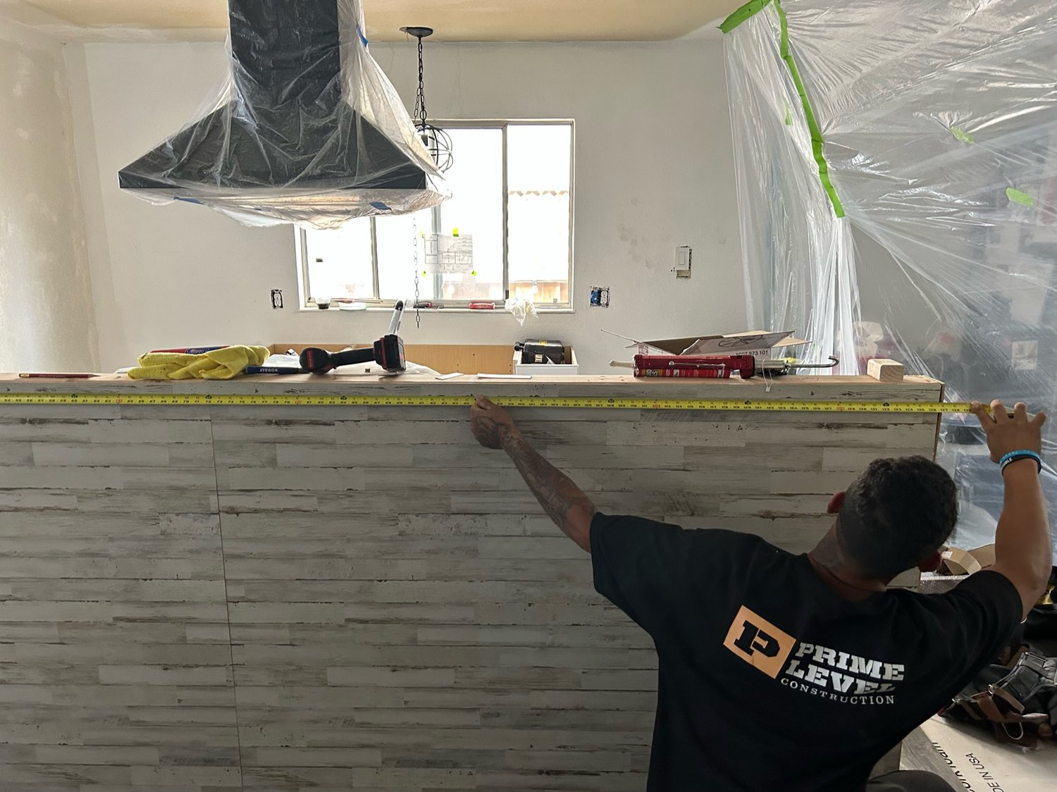 Construction worker from Prime Level Construction measuring a kitchen installation with a tape measure in a partly renovated room in Santa Rosa.