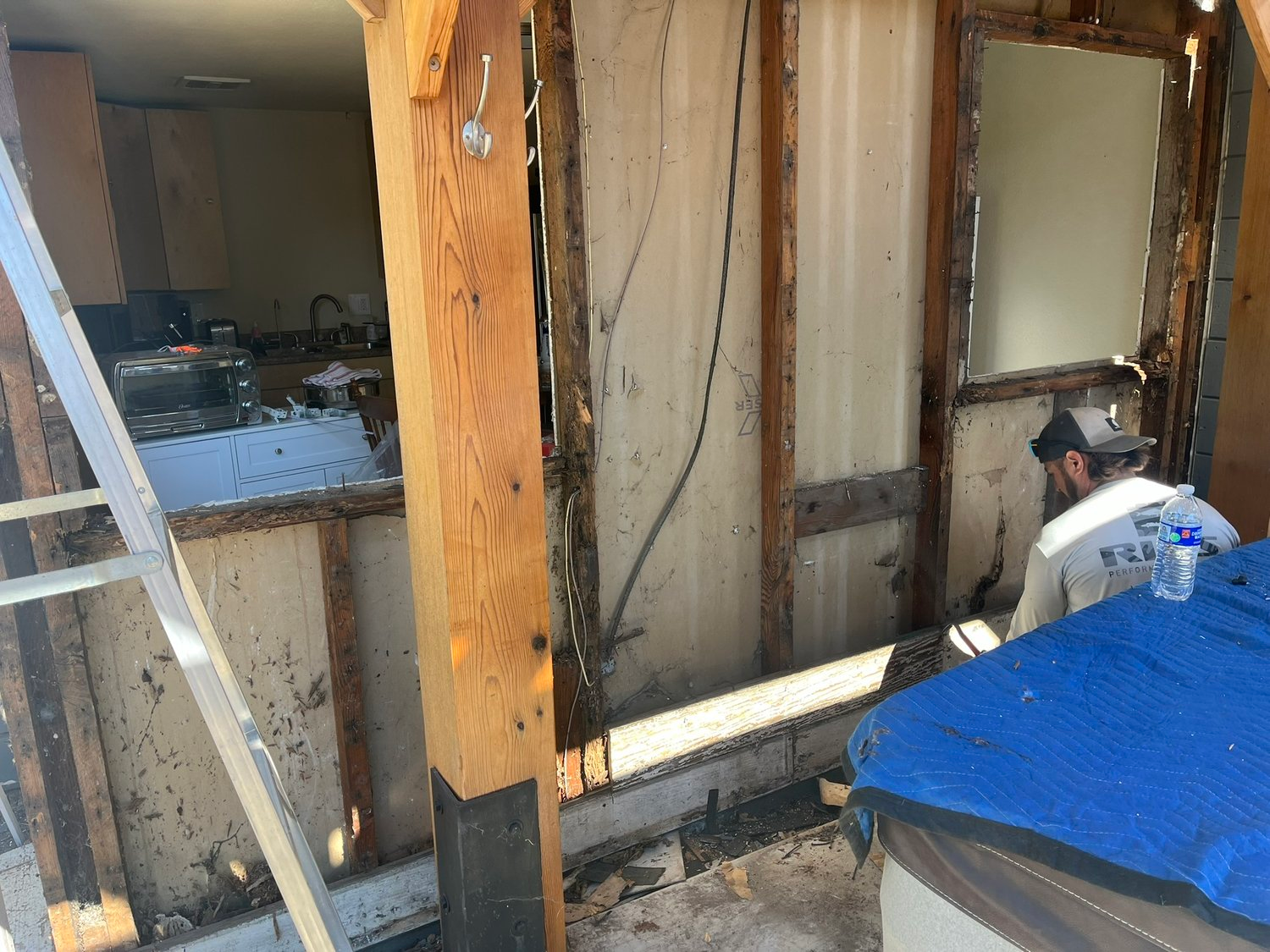 "A worker from Prime Level Construction in Santa Rosa repairing a damaged wall with exposed wooden beams, showcasing renovation work in progress."