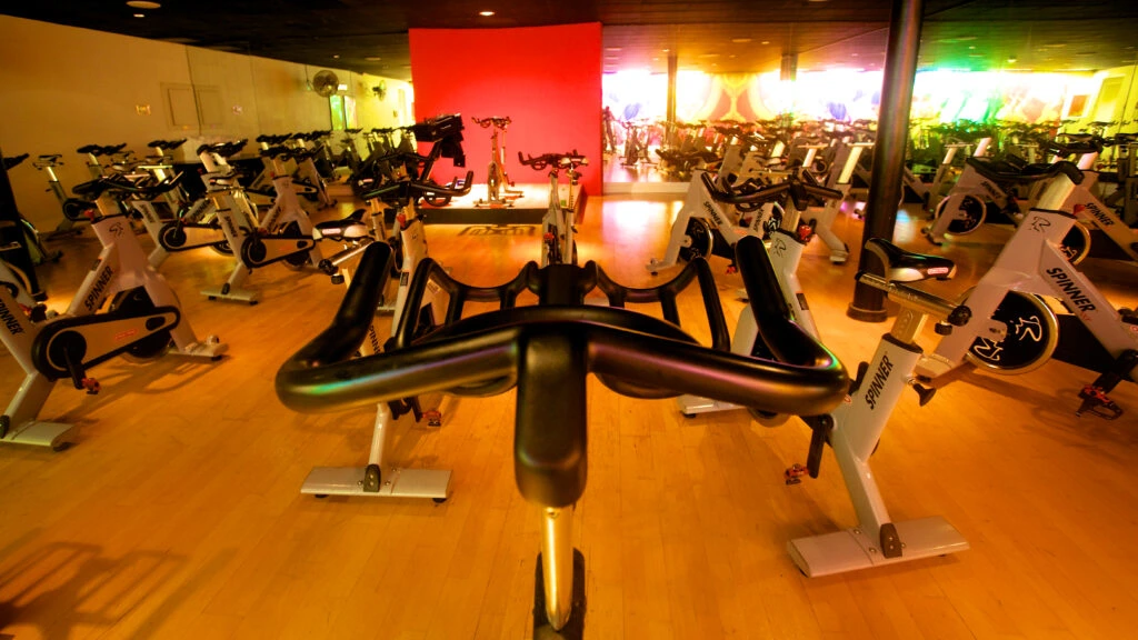A brightly lit indoor cycling studio at Prime Time Athletic Club in Burlingame, featuring rows of stationary bikes on a wooden floor.