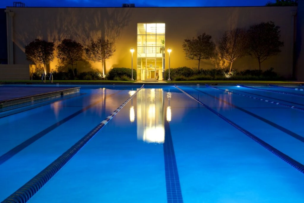 Illuminated swimming pool at Prime Time Athletic Club in Burlingame at night, with lights reflecting in the water.