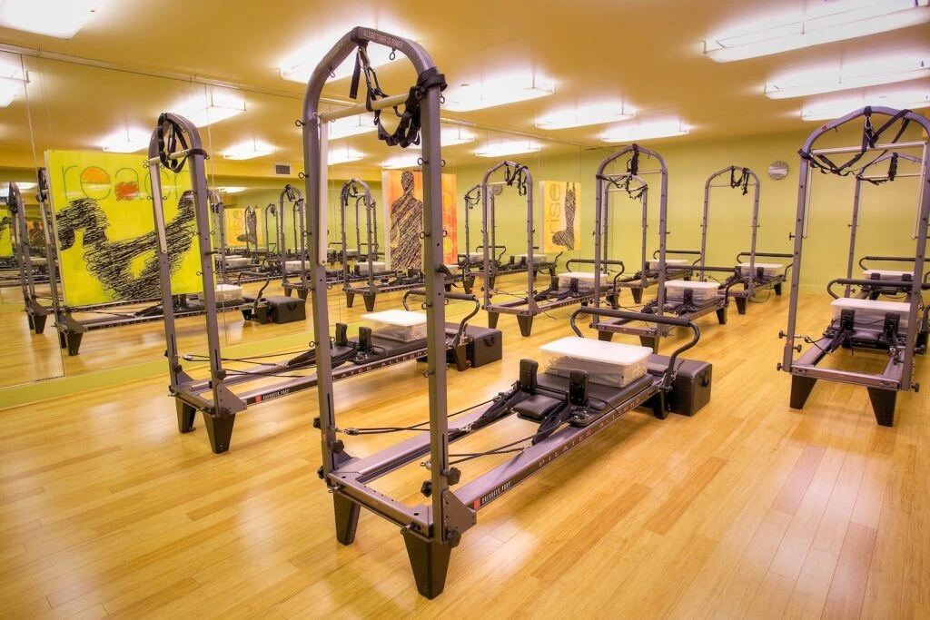 A bright studio at Prime Time Athletic Club in Burlingame featuring multiple Pilates reformers, wooden flooring, and mirrored walls.