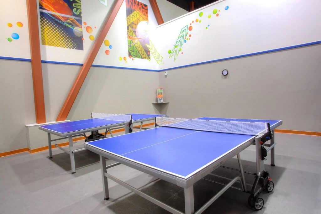 Two blue table tennis tables with nets in a spacious room with colorful wall decorations at Prime Time Athletic Club, Burlingame.