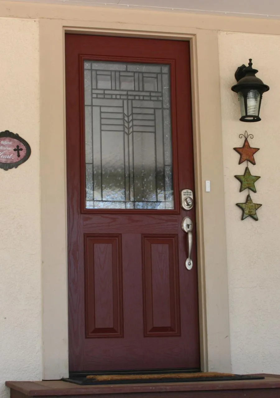 A red front door with decorative glass and a modern lock system, accompanied by a wall lamp and star-shaped decorations.
