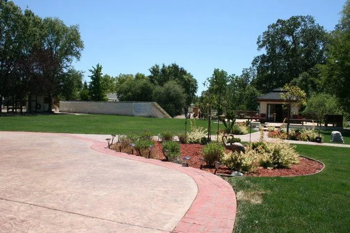 A beautifully landscaped backyard with a curved paved pathway, manicured lawn, planted flower beds, and a gazebo, showcasing Quality First Home Improvement, Inc.'s work in Citrus Heights.