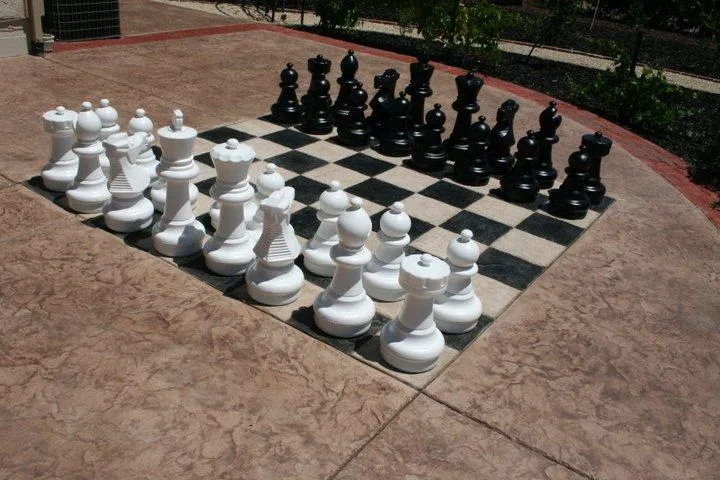 Large outdoor chess set with black and white pieces on a checkered stone board, shown in a garden setting, highlighting Quality First Home Improvement, Inc.'s craftsmanship in Citrus Heights.