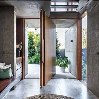 A modern interior with an open large wooden door, showcasing an entrance to a garden with greenery, designed by Quality Windows & Doors, Inc. in Pleasanton.