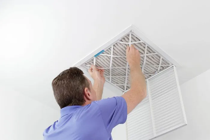 A technician in a blue shirt replaces an air filter in a ceiling vent, representing Qualtech Heating & Cooling's services in Danville.