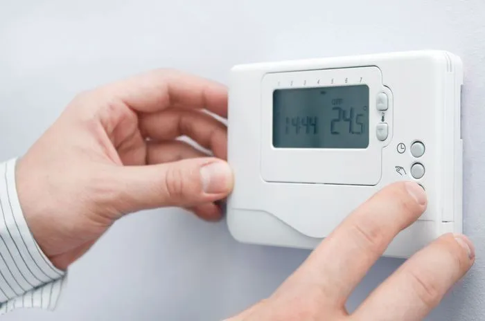 A person adjusts a digital thermostat on a wall, highlighting energy control, associated with Qualtech Heating & Cooling in Danville.