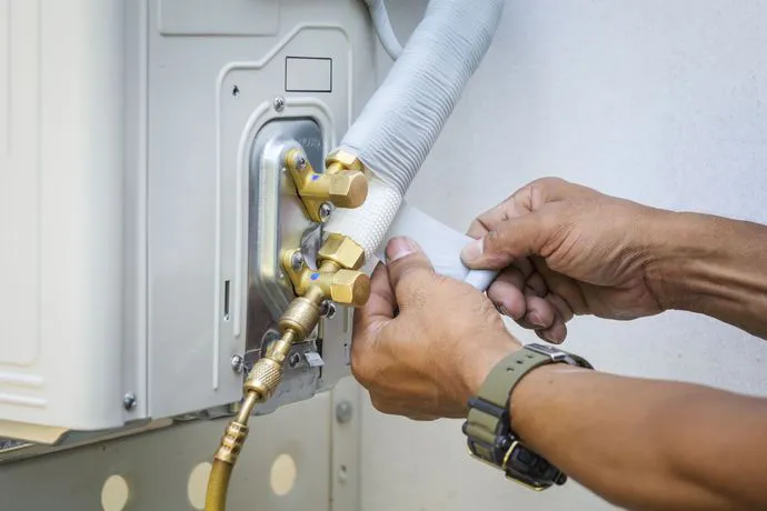 A technician's hands from Qualtech Heating & Cooling in Danville adjusting air conditioning components, demonstrating intricate HVAC maintenance.