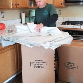 "A man packing items into a box labeled 'Fragile' in a kitchen, demonstrating the packing services of Quantum Moving in Martinez."