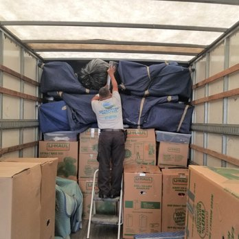 An individual from Quantum Moving in Martinez expertly organizes boxes and furniture padding inside a moving truck, highlighting their efficient packing skills.